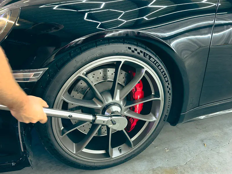 A Superior Autohaus mechanic tightening the hubcap onto a black Porsche 911.