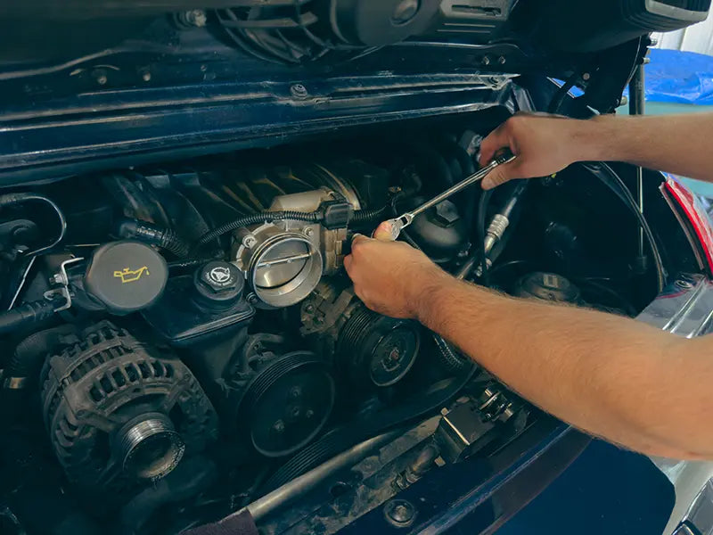 A Superior Autohaus mechanic working on the engine of a dark green Porsche 911.