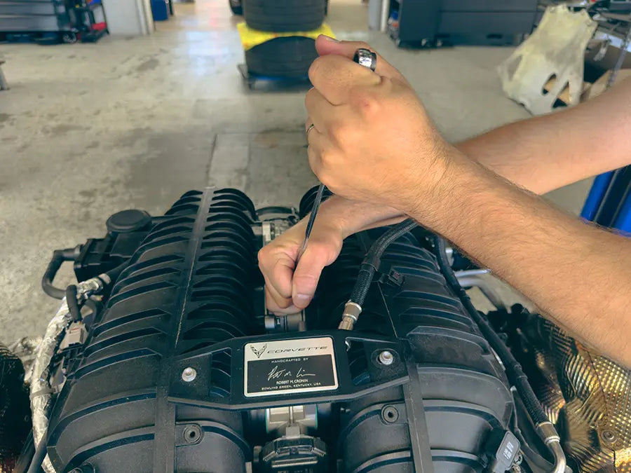 A Superior Autohaus mechanic working on a Chevrolet Corvette engine using a wrench.