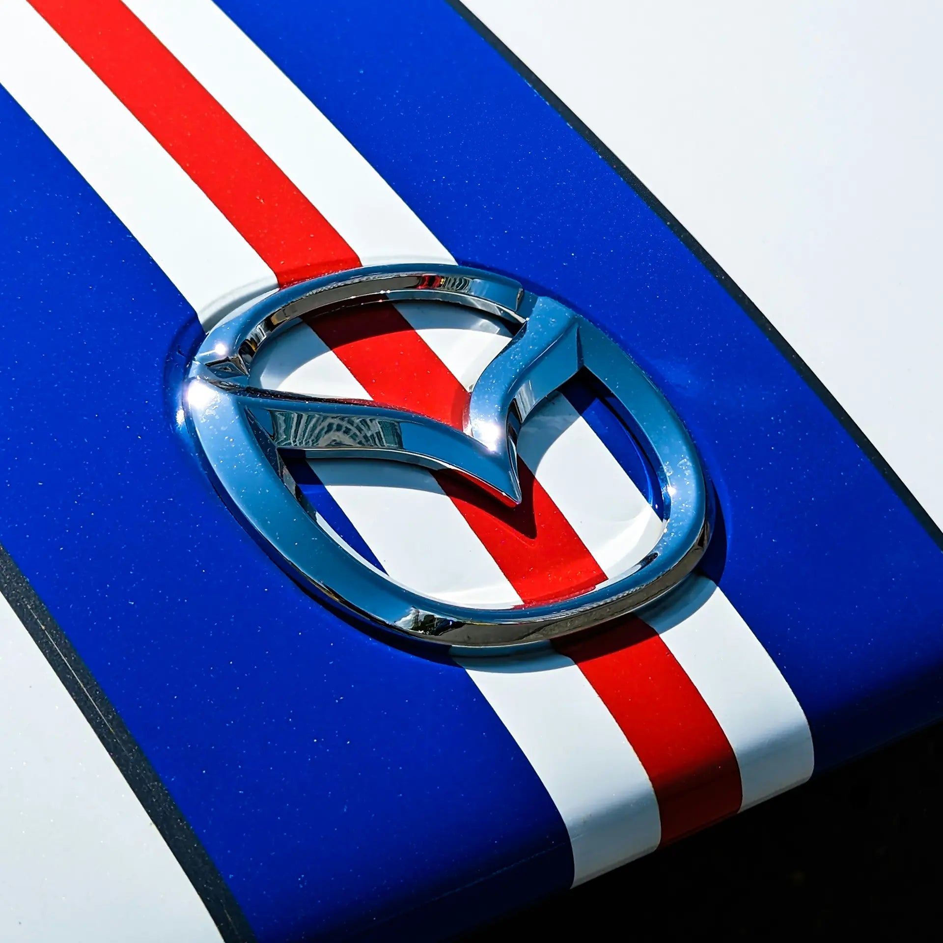 Mazda badge on a white car with blue and red stripes. 