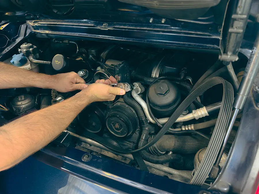 A Superior Autohaus mechanic working on the engine of a dark green Porsche. 
